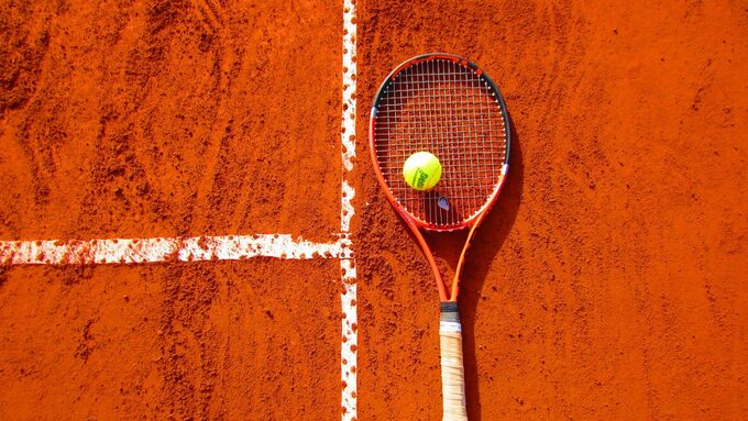 Une raquette de tennis posée par terre sur un terrain sportif d'argile.